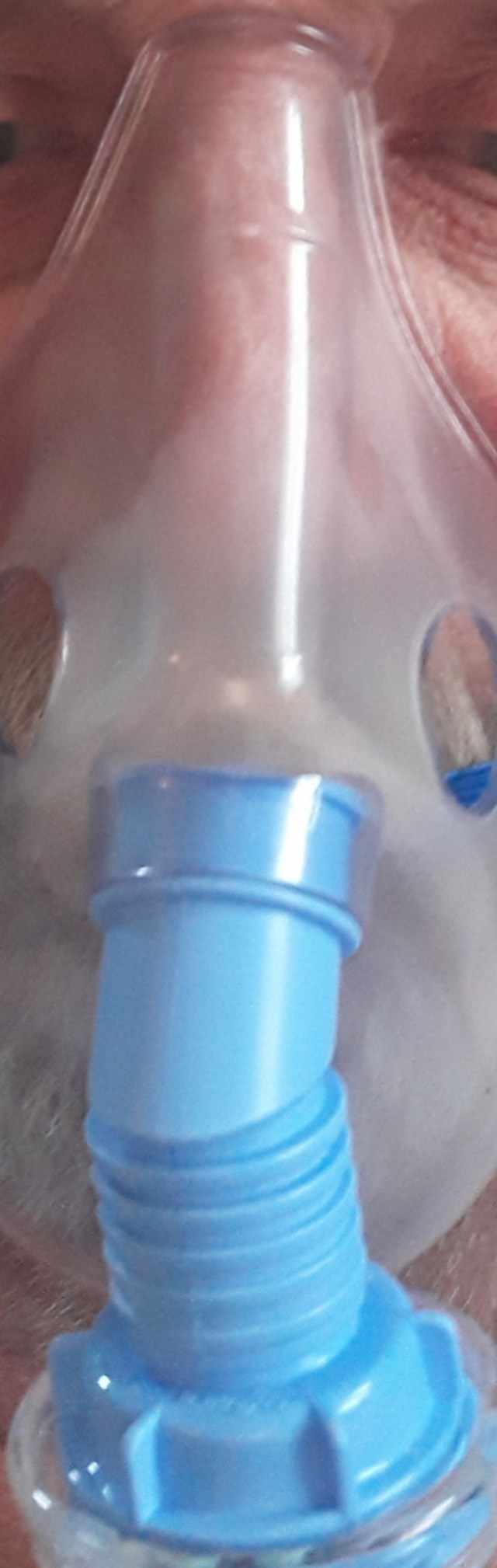 Image of a face using a nebuliser with a blue plastic attachment. Partial view of the eyes and a grey beard behind the nebuliser.