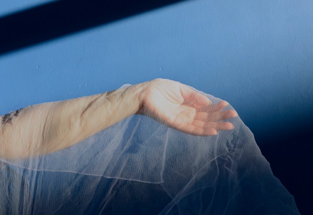 Image of a hand and arm, covered with white gauze material, against a blue background.