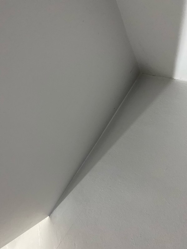 Photo of the corner of a ceiling, painted white, with a slight shadow.